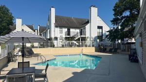 einen Pool mit Stühlen und einem Sonnenschirm neben einem Haus in der Unterkunft Sonesta ES Suites Cincinnati - Sharonville West in Sharonville