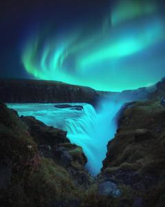an aurora over a river with a waterfall at Cosy apartment Central Kopavogur in Reykjavík