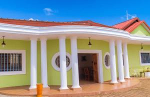 a green house with white columns and a red roof at Hôtel chez Marie Oyouma in Port-Gentil