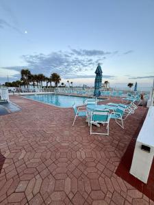 Un grupo de sillas y mesas junto a una piscina. en SeaBliss, oceanfront 1st floor cozy condo, en Daytona Beach