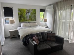 a bedroom with a bed and a leather couch at Peaceful house in Kumeu
