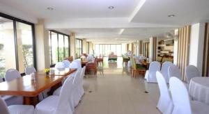 サコンナコーンにあるPC Palace Hotelの白い椅子と長いテーブルとテーブルと椅子のあるダイニングルーム