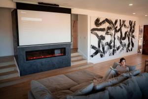 a woman sitting on a couch in front of a large screen at Mountain Views, Pool, Spa & Serenity Stargate in Yucca Valley