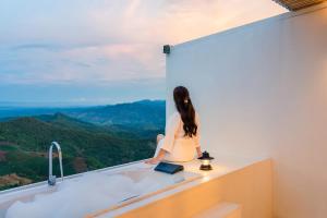Eine Frau sitzt auf einer Theke und schaut aus dem Fenster in der Unterkunft Arroon Chiang Rai, Thailand in Ban San Pu Loei