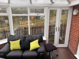 Un sofá negro con almohadas amarillas en un porche. en Valley View Guest House, en Newcastle-under-Lyme