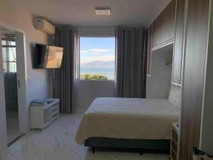 a hotel room with a bed and a large window at Loft vista incrível beira mar continental in Florianópolis