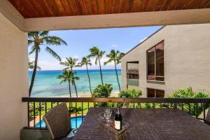 a table with wine glasses on a balcony with the ocean at Hale Mahina B401 · HM B401 OceanFront 2BD Tropical Getaway in Kahana