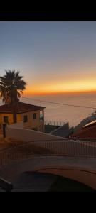 un coucher de soleil sur l'océan avec un bâtiment et un palmier dans l'établissement Beautiful View - Arco da Calheta - Ilha da Madeira, à Arco da Calheta