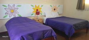 two beds in a room with purple sheets and flowers on the wall at Kurumi Hostel in Cusco
