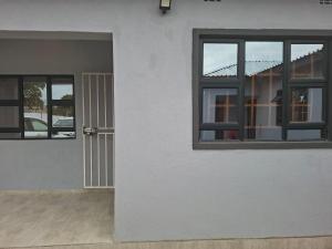 ein weißes Haus mit zwei Fenstern und einer Tür in der Unterkunft Cosy Cottage Apartments ,Area L in Francistown