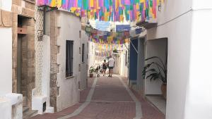 a narrow alley with colorful flags and people walking down it at Calamora-Moraira in Moraira