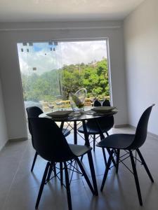 サン・ミゲル・ドス・ミラーグレスにあるCasa 2 quartos com área verde AnaManô Suitesの大きな窓のある部屋にあるテーブルと椅子