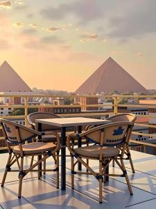 a table and chairs on a roof with pyramids in the background at Pyramids & SphinX Grand Hotel in Cairo
