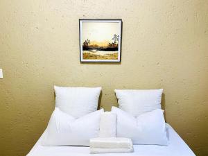 ein Bett mit weißen Kissen und einem Bild an der Wand in der Unterkunft Sandton Skyline Suite - 2 Bedroom Apartment in Sandton