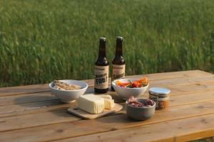 two bottles of beer and bowls of food on a wooden table at Parcel Tiny House Vallée, près de Verdun in Rarécourt