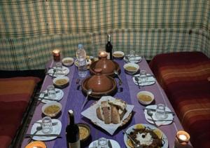 a table with a purple table cloth with food and drinks at Sahara horizon Camp in Merzouga +36 photos