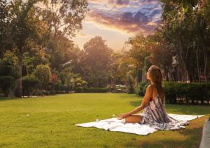 a woman sitting on a blanket in the grass at Narayana Sanctuary Resort by SALVUS in Rishīkesh