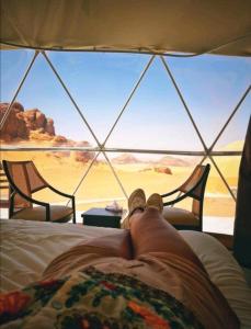 a person laying on a bed looking out at the desert at mountains wadi rum in Disah