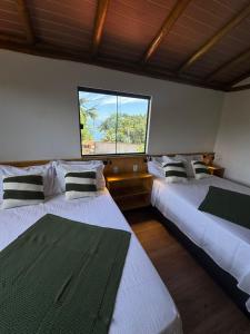 two beds in a room with a large window at Pousada Tropical Araçatiba in Praia de Araçatiba