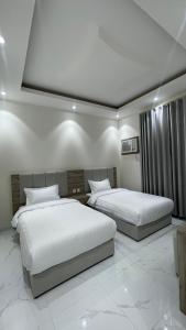 two beds in a bedroom with white walls and white floors at شقق واڤا in Tabuk