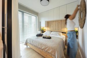 Una mujer está de pie en un dormitorio con una cama. en Marina Ostróda III - widok na jezioro, podziemny garaż, winda, klimatyzacja, wanna i prysznic, 2 łazienki, lux, en Ostróda