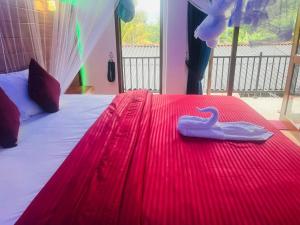 un lit rouge avec une serviette de plage à motif cygne dessus dans l'établissement Ella EDAN Homestay, à Ella