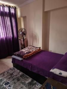 une chambre avec un lit avec des draps violets et un ventilateur dans l'établissement Taher Cairo Hostel, au Caire
