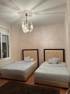 two beds in a bedroom with a chandelier at Résidence BAB Sebta apartment Ghali in Fnidek +24 photos