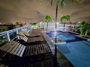 un balcone con due panchine e una piscina di notte di Apto em Zona Nobre à Beira-mar com Piscina, Ar Condicionado, Garagem GRÁTIS a Maceió