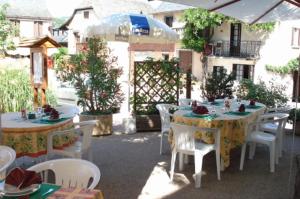 un patio al aire libre con mesas, sillas y una sombrilla en Auberge Aux Portes de Conques, en Saint-Cyprien-sur-Dourdou