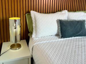 ein Bett mit weißer Bettwäsche und einer Lampe auf einem Nachttisch in der Unterkunft Casa Trindade - Residencial Caminho da Praia in Porto Seguro