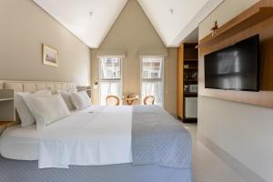 a bedroom with a white bed and a flat screen tv at Vilinha típica - Suíte Onze Tuin - Entrada com senha - Somos hospedagem por temporada in Holambra