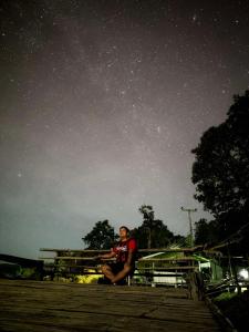 un homme assis sur un toit sous un ciel étoilé dans l'établissement Homestay Nunga หนูหง่าโฮมสเตย์คุณครู, à Mae Hong Son
