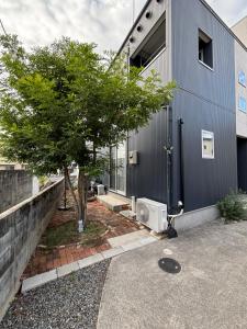 a gray house with a tree in front of it at 一棟貸切の民宿 月 駐車場2台無料 バス停徒歩1分 市街地へ好アクセス in Matsuyama