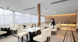 GuzhutingにあるVienna Hotel Yongzhou Dong'an High-Speed Railway Stationのテーブルと椅子のあるレストランに立っている女性