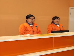zwei Frauen in orangefarbenen Jacken, die an einem Tresen sitzen in der Unterkunft 7 Days Inn Luzhou Longma Avenue District Government in Luzhou