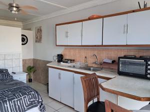 een keuken met witte kasten, een wastafel en een bed bij Lion's Cave 1B in Mosselbaai