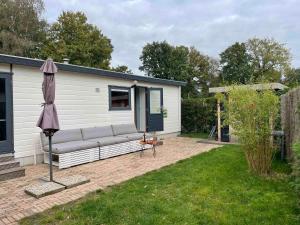 un patio con divano e ombrellone in un cortile di Kleurrijk boshuisje Sole op de Veluwe a Putten