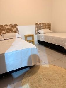 two beds in a room with a rug and a table at Pousada Amarílis in Barra de Santo Antônio