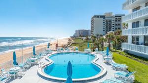 een zwembad met stoelen en parasols naast een strand bij Ormond Beach Paradise - Steps from no-drive beach in Ormond Beach