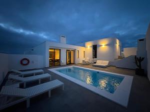 ein großer Swimmingpool mit zwei weißen Bänken neben einem Haus in der Unterkunft Casa Blanca - Villa à Teguise avec piscine privée in Teguise