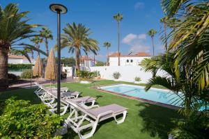 une piscine avec des chaises longues et des palmiers dans l'établissement Villa Maspalomas Golf Court, à Maspalomas