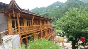 a wooden building with a balcony and a tree at Xiangtule Inn in Xinglong