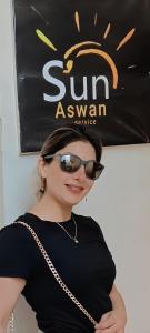 Uma mulher usando óculos de sol em pé em frente a uma placa. em Sun Aswan inn em Aswan