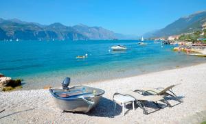 - un bateau et des chaises sur une plage au bord de l'eau dans l'établissement Hotel Du Lac - Relax Attitude Hotel, à Brenzone