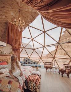 Una mujer sentada en una cama en una habitación con una ventana grande. en MOON RUM lUXURY CAMP, en Wadi Rum