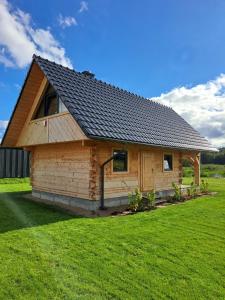 eine Blockhütte mit schwarzem Dach auf einer grünen Wiese in der Unterkunft Drewno i Len in Debina