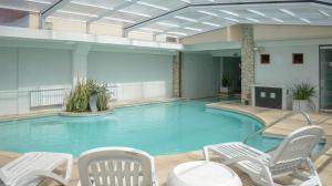 a large swimming pool with white chairs and a table andermottermott at Fonte Arcada in Villa Gesell