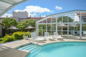 a swimming pool with two chairs and a glass house at Fonte Arcada in Villa Gesell