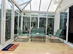 a conservatory with two green chairs and a table and windows at Crescent House - 3 Bedrooms, 2 bathrooms, large lounge, sunny conservatory, full kitchen, parking for 2 cars in Buckinghamshire